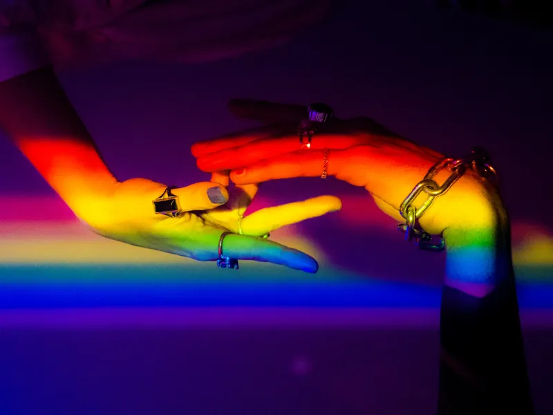 Two hands reaching toward each other in rainbow light